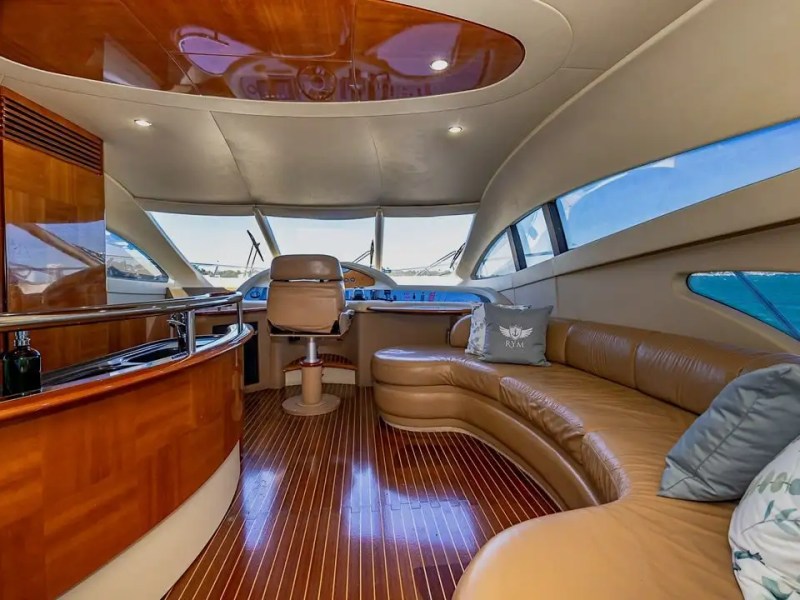 Luxurious yacht interior with wood paneling, curved leather seating, and large windows revealing blue sea.