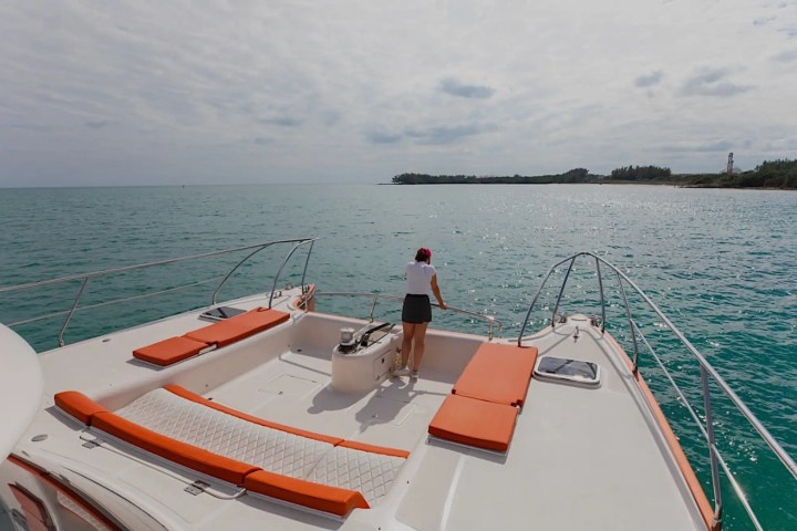 Person on boat deck overlooking ocean near a coastline on a cloudy day.