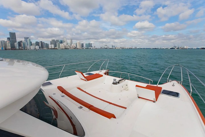 View from a yacht deck with orange seating, city skyline and ocean under a cloudy sky.