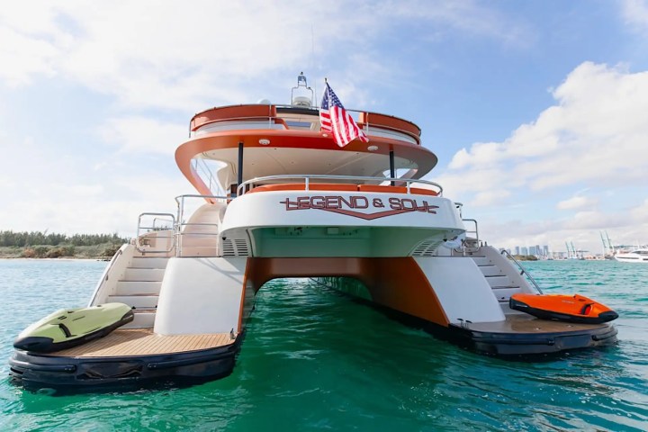 Luxury yacht 'Legend & Soul' with American flag, docked at sea with water toys on platforms.