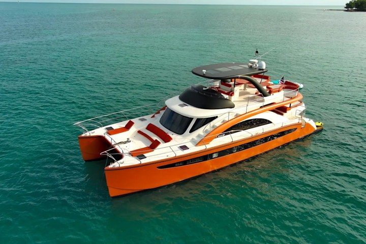 Orange and white catamaran yacht on clear blue water.