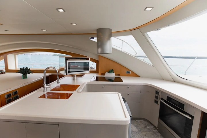 Modern yacht kitchen with sleek countertops, oven, sink, and large windows overlooking the ocean.