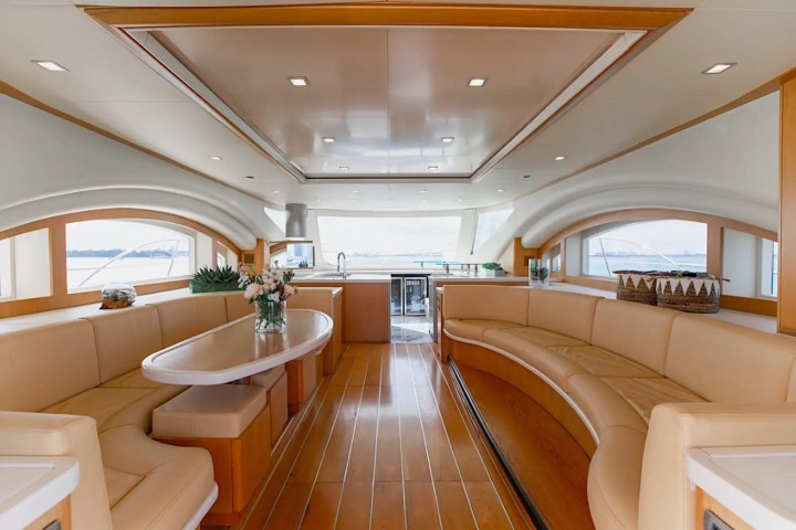 Luxurious yacht interior with cream leather seats, wood flooring, and large windows.