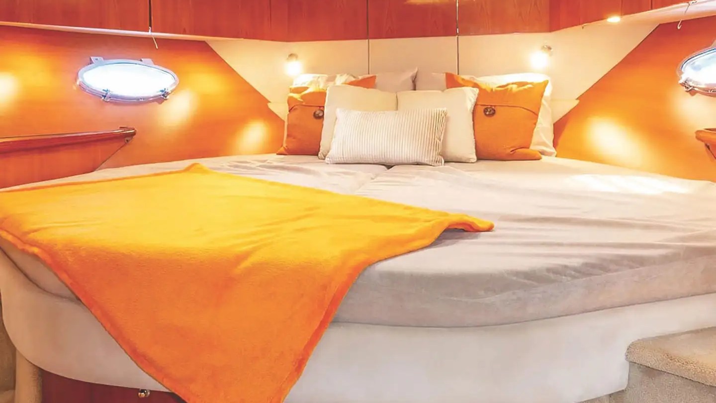 Cozy boat cabin with orange and white bed, pillows, and dim lighting.