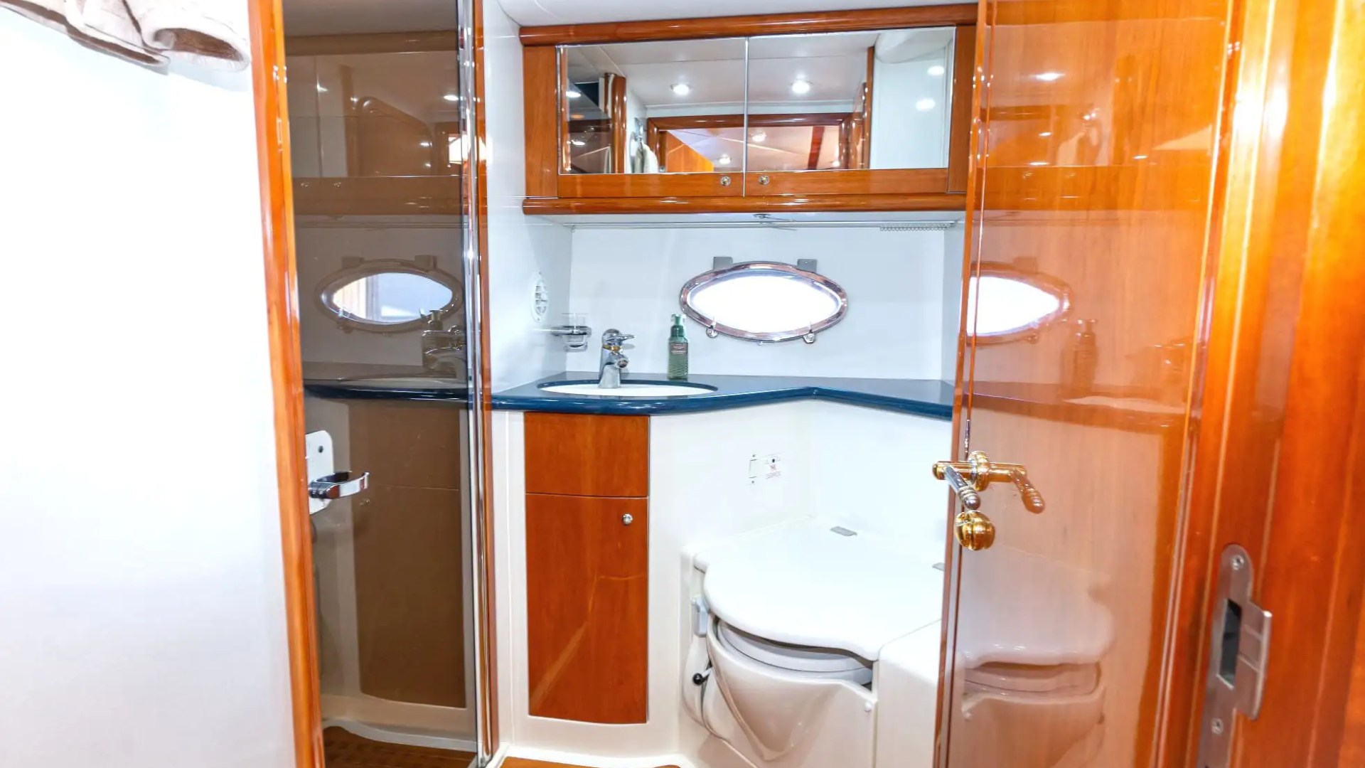 Compact yacht bathroom with wood accents, shower, sink, and small porthole window.