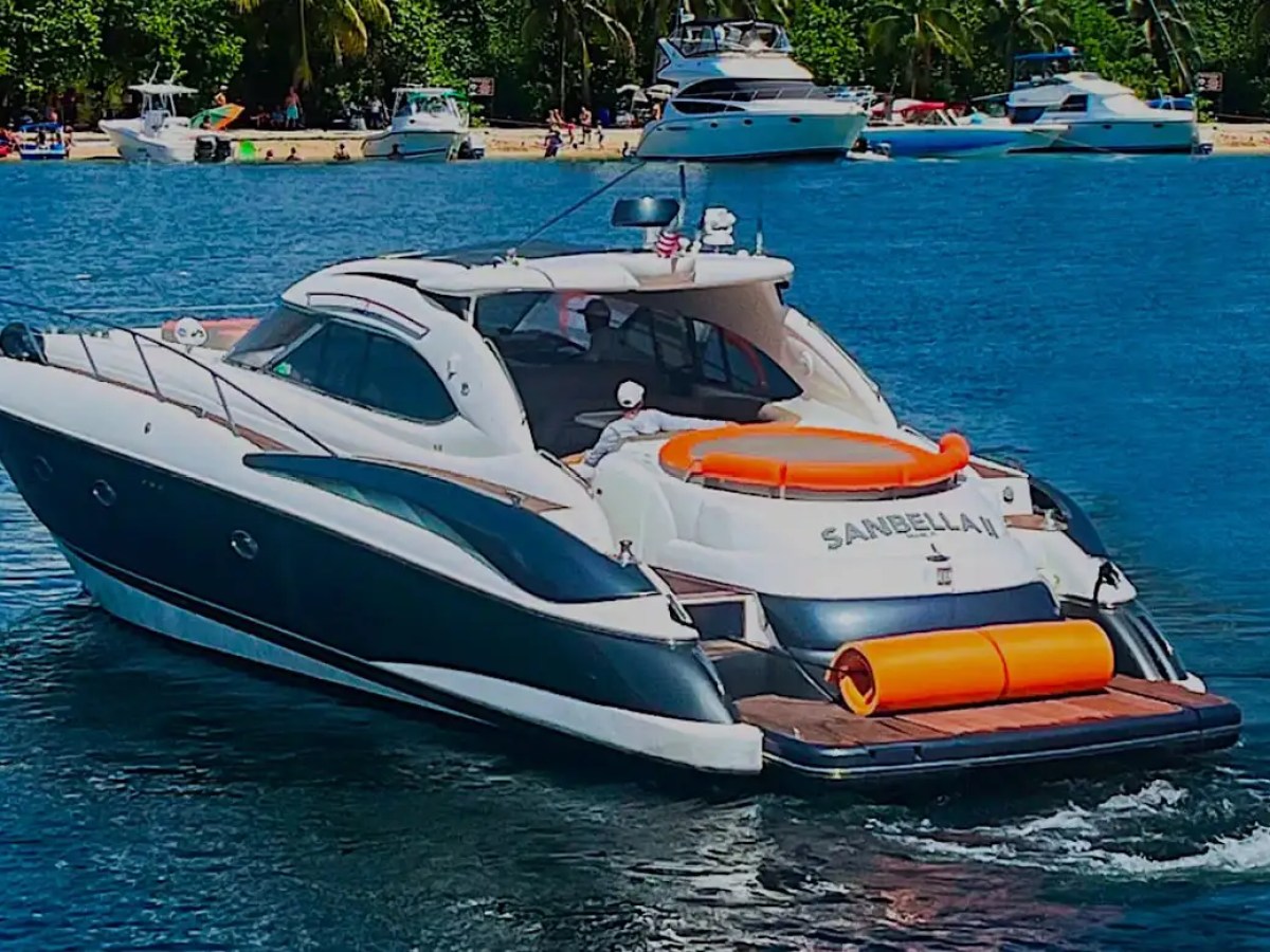 A yacht on the water with a beach and other boats in the background.