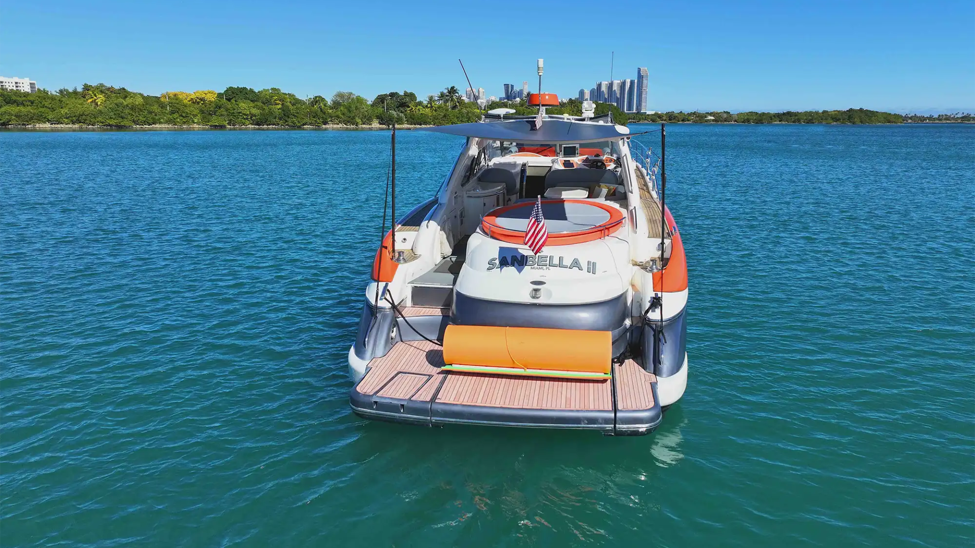 Luxury yacht on blue water with cityscape and greenery in the background under clear blue sky.