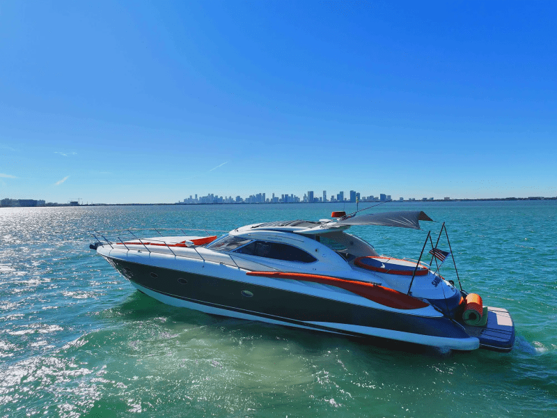 Yacht on a blue ocean with a city skyline in the background on a sunny day.