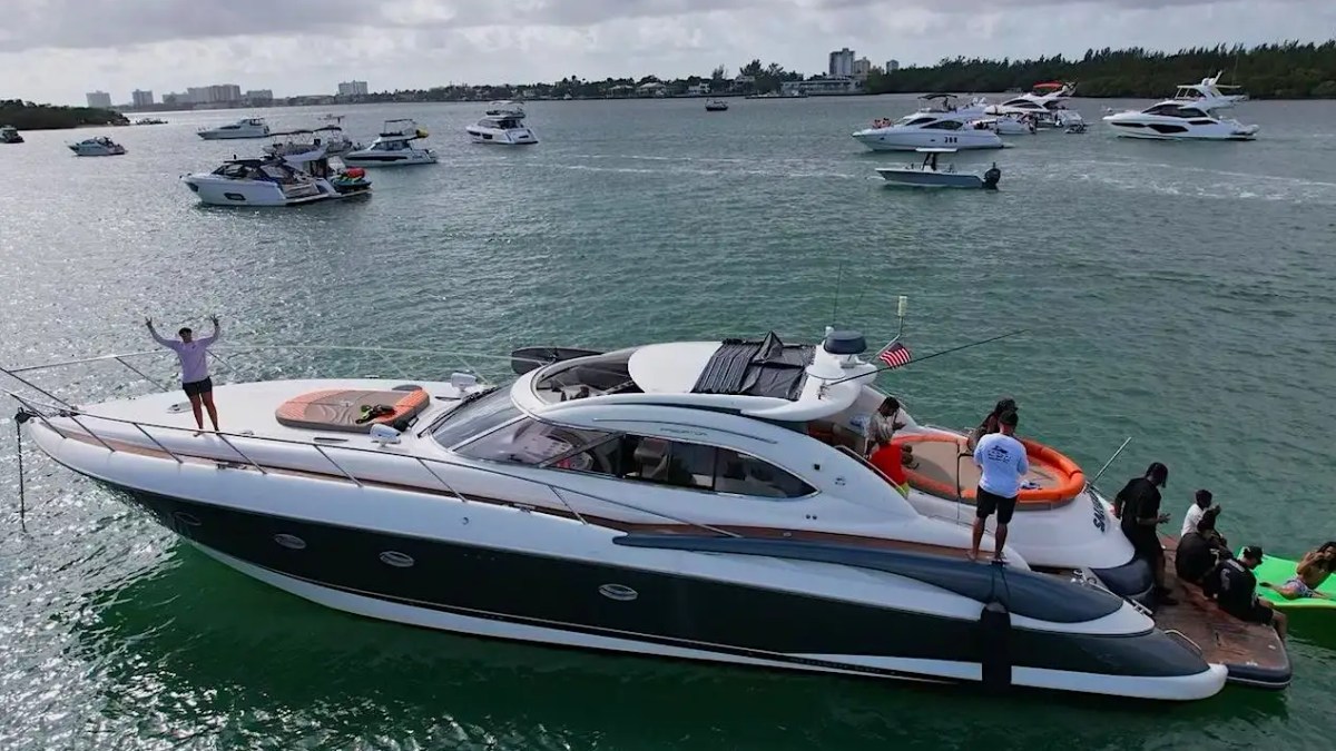 Luxury yacht anchored in a bay crowded with several boats on a cloudy day.