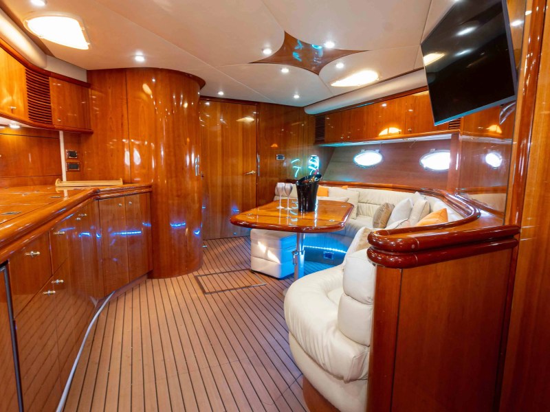 Luxurious yacht interior with wooden decor, curved sofa, table, and TV.