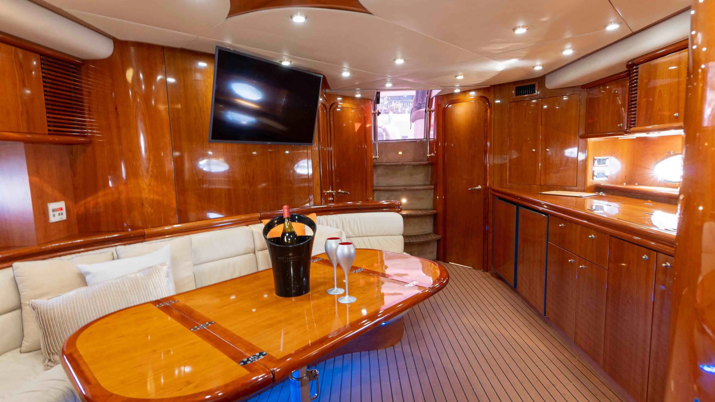 Luxurious yacht interior with wooden decor, seating, a table, and a mounted TV.