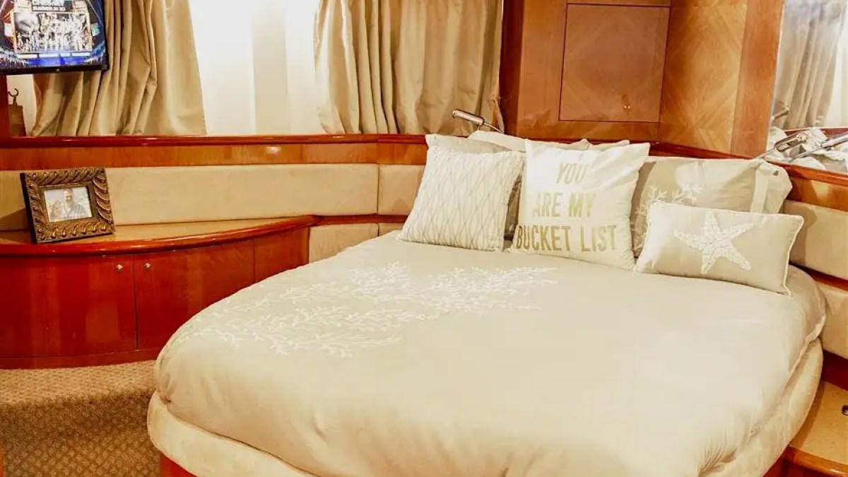 Luxurious yacht cabin with a round bed, pillows, and framed photo; TV screen displays a scene.
