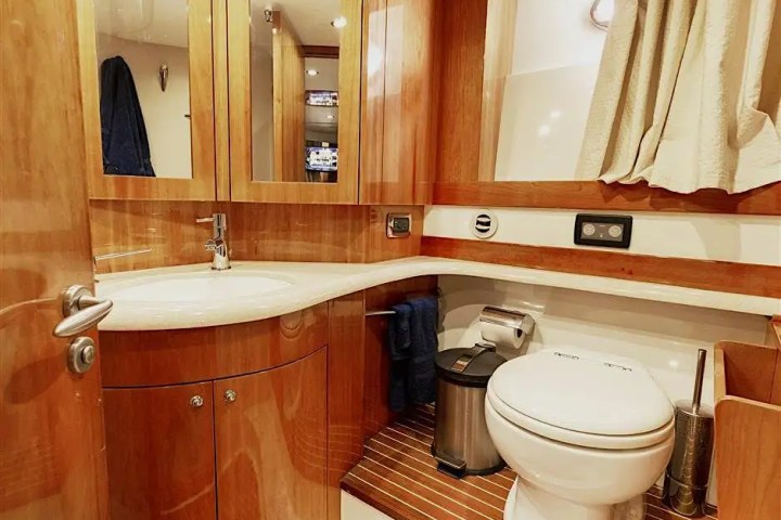 Wood-paneled bathroom with a round toilet, sink, mirrored cabinets, and striped flooring.