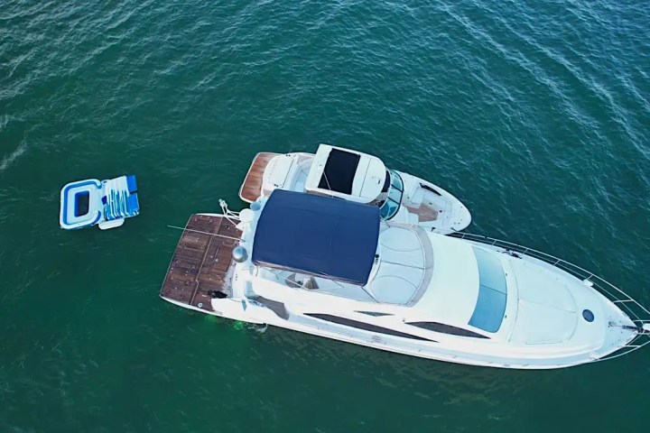 Aerial view of a white yacht on green water with an inflatable floating nearby.