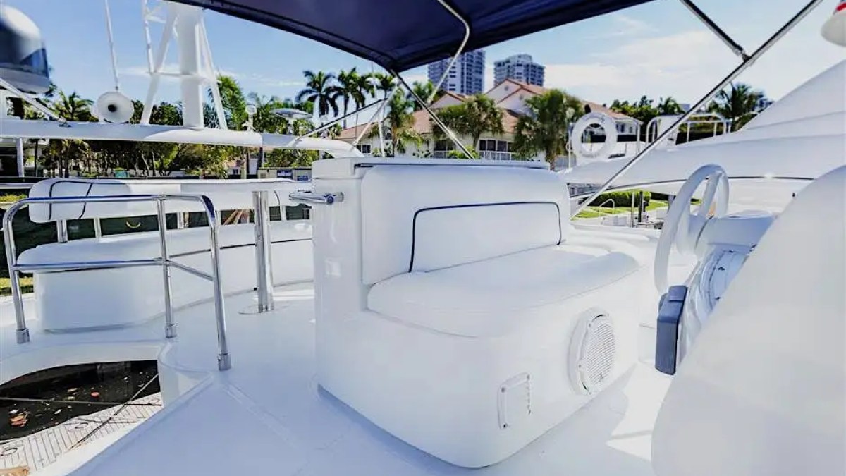 Boat deck with white seating and helm under a blue canopy on a sunny day.