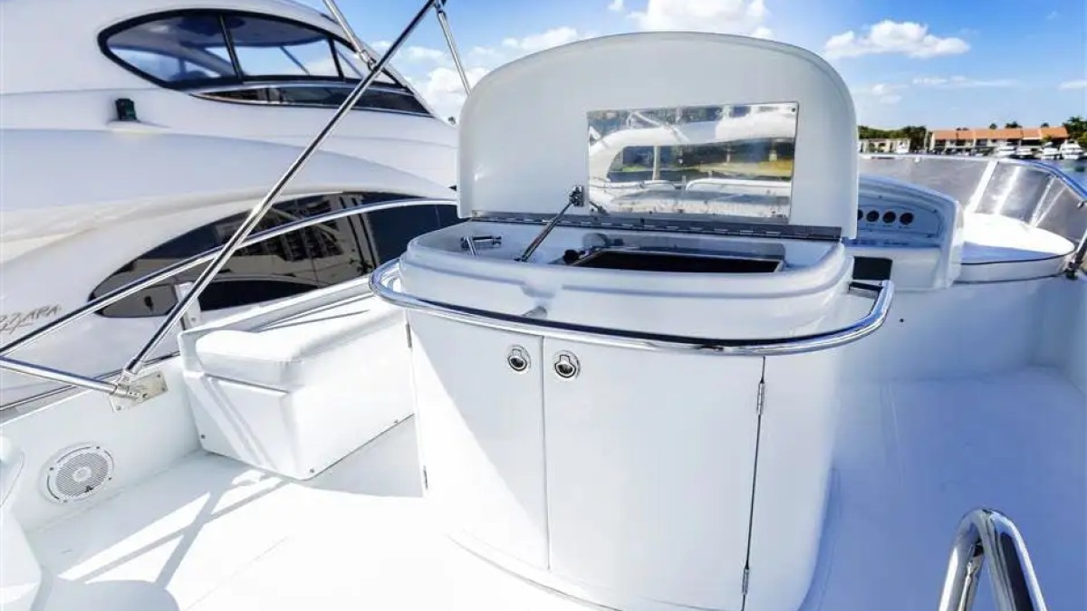White yacht deck with built-in bar under blue sky, marina in background.