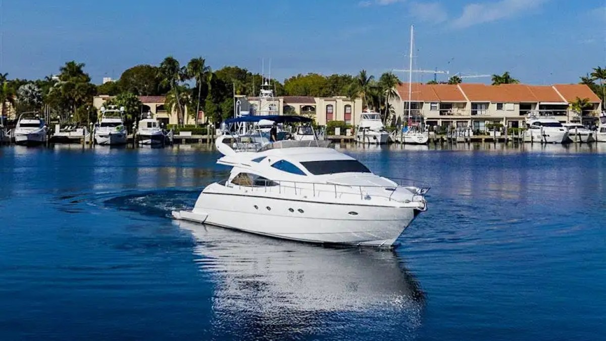White yacht on a calm blue waterway with houses and trees in the background.