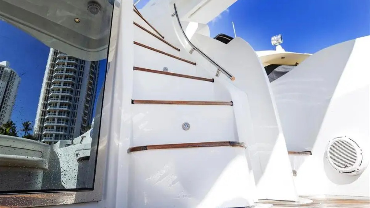 View of yacht stairs with wooden steps and reflection of building in glass under a clear blue sky.