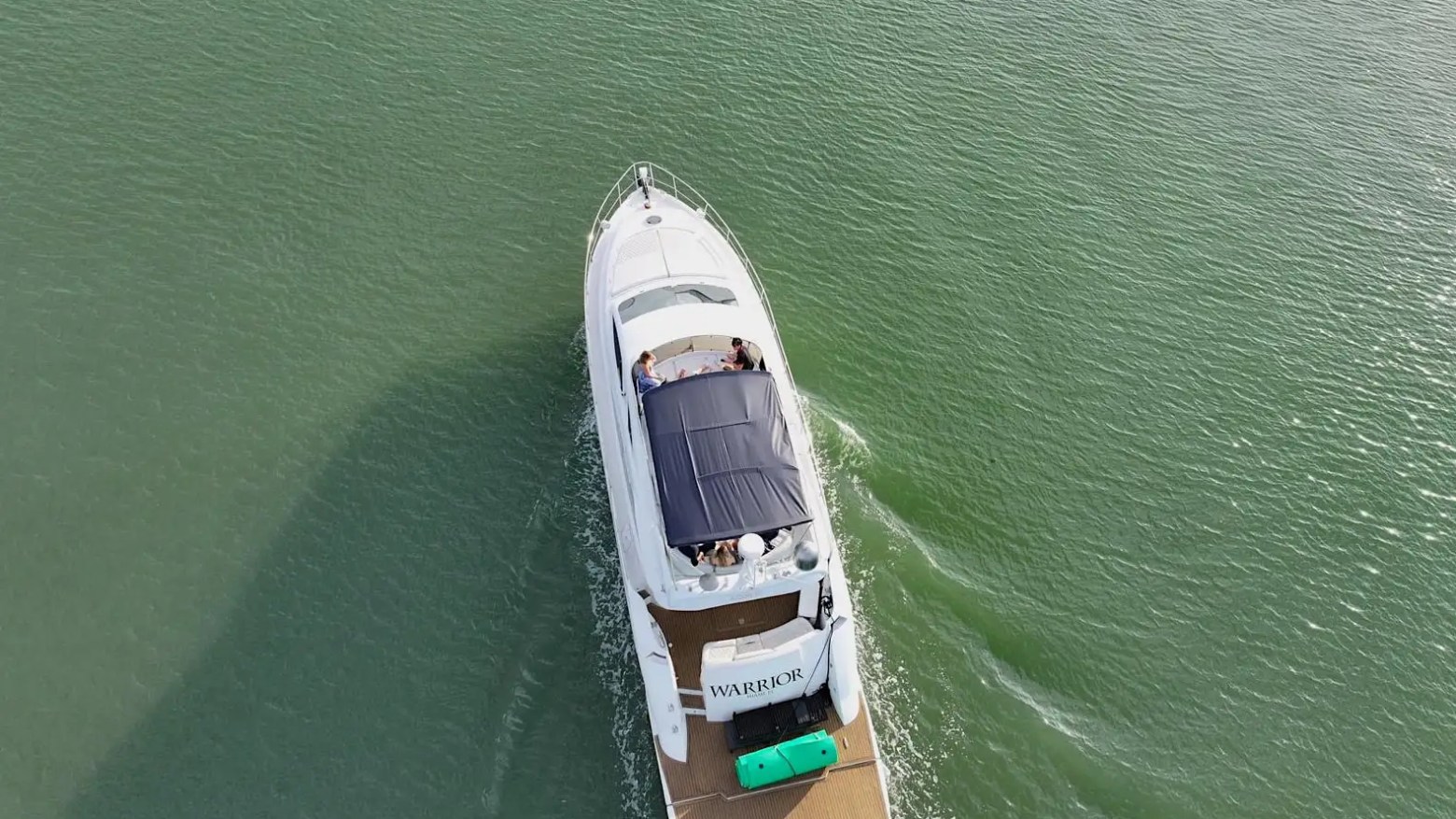 Aerial view of a white yacht named 'Warrior' cruising on green water.