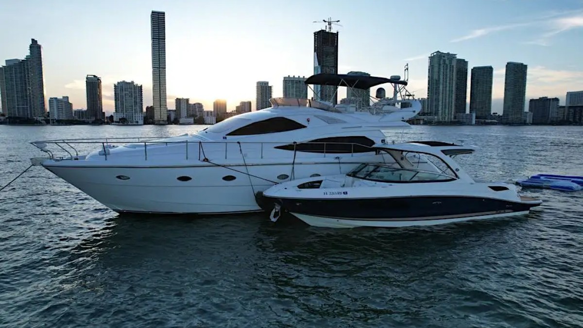 Two yachts docked together with a city skyline in the background at sunset.