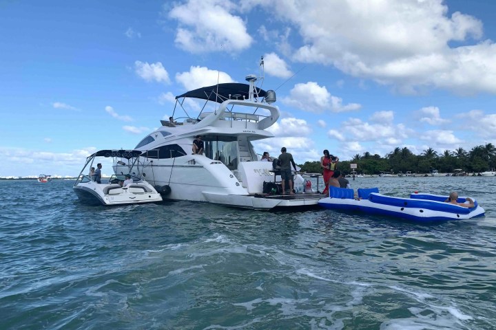 Two boats on the water with people and an inflatable raft nearby under a blue sky.
