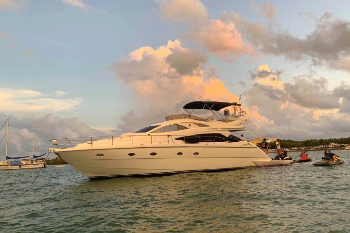 Luxury yacht on water during sunset with people on jet skis nearby.