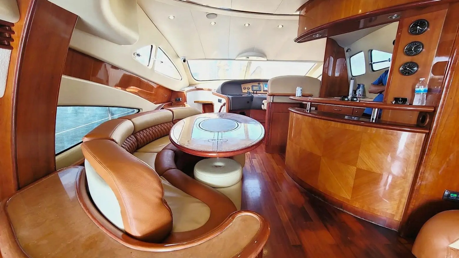 Luxurious yacht interior with curved leather seating, wooden tables, and bar area.