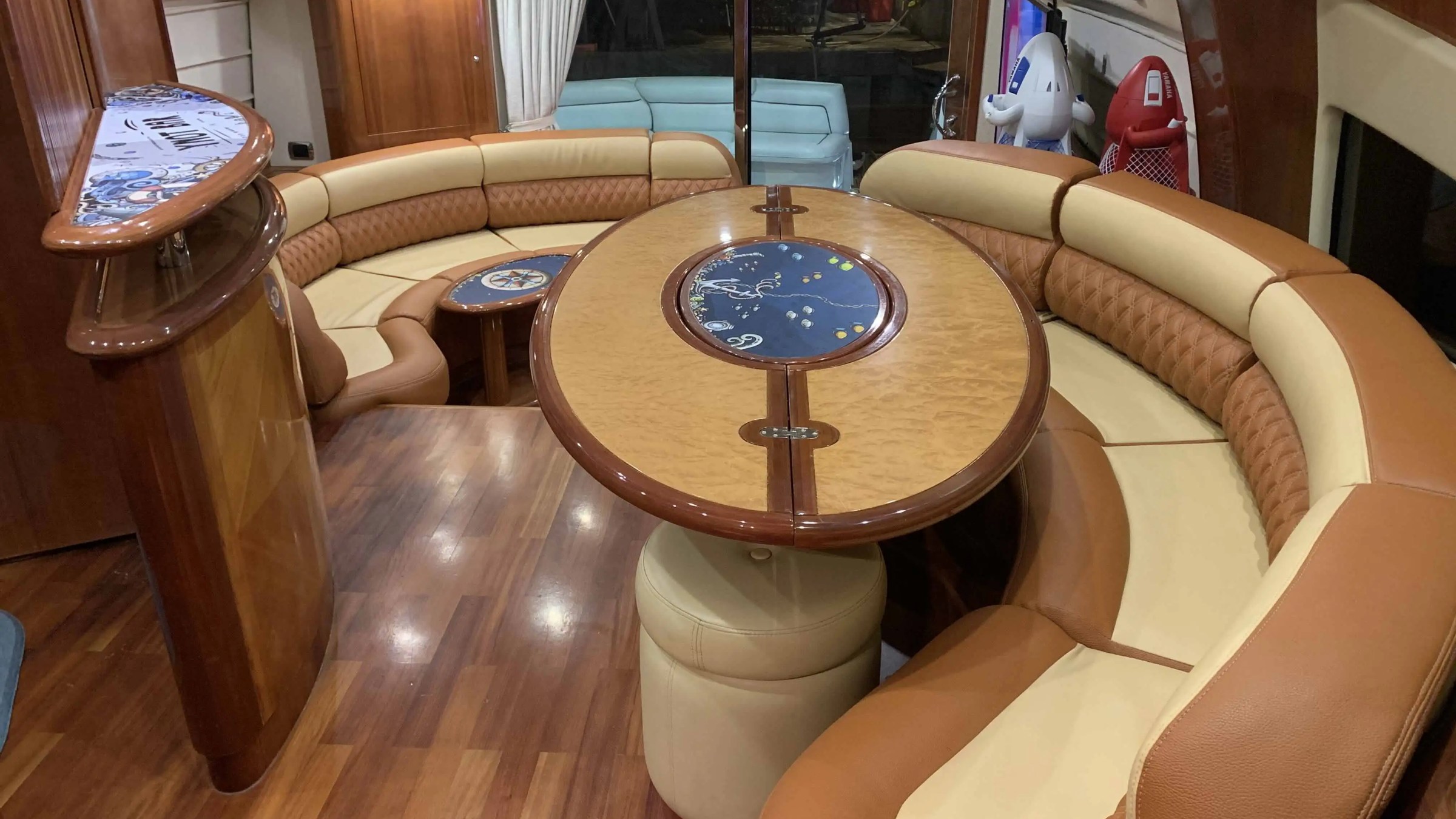 Luxurious yacht interior with curved seating, wooden table, and bar area.