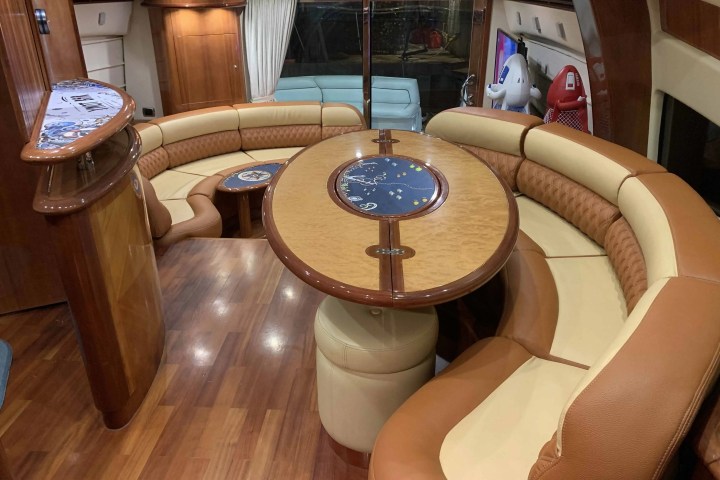 Luxurious yacht interior with curved seating, wooden table, and bar area.