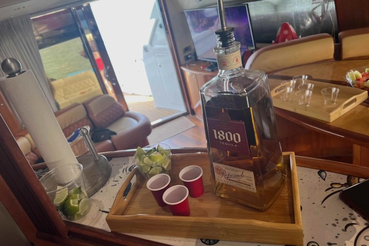Tequila bottle with limes and red cups on tray in boat interior.