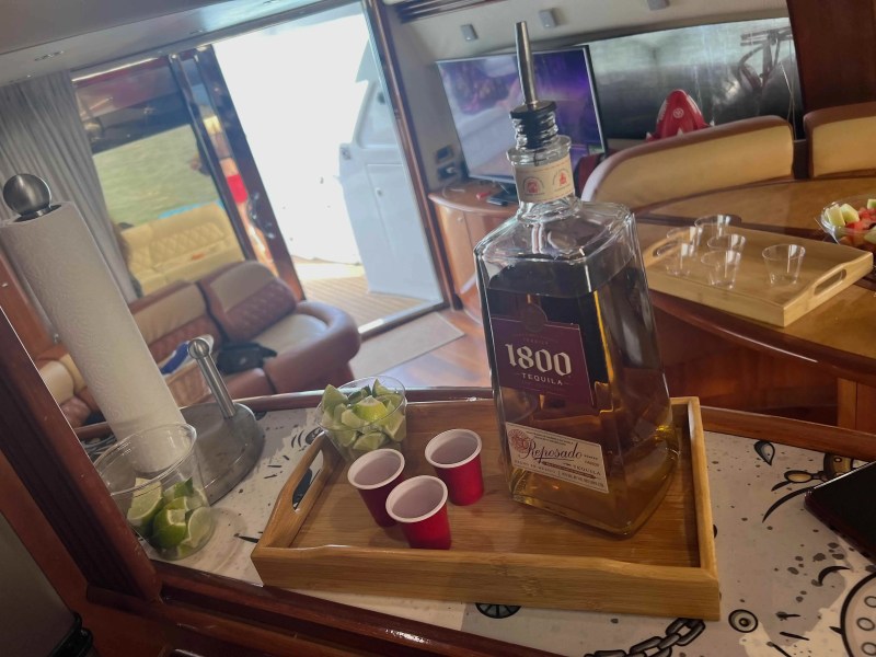 Tequila bottle with limes and red cups on tray in boat interior.