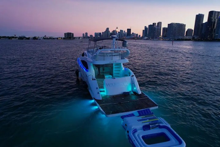 Lit yacht on water at dusk with city skyline in the background.