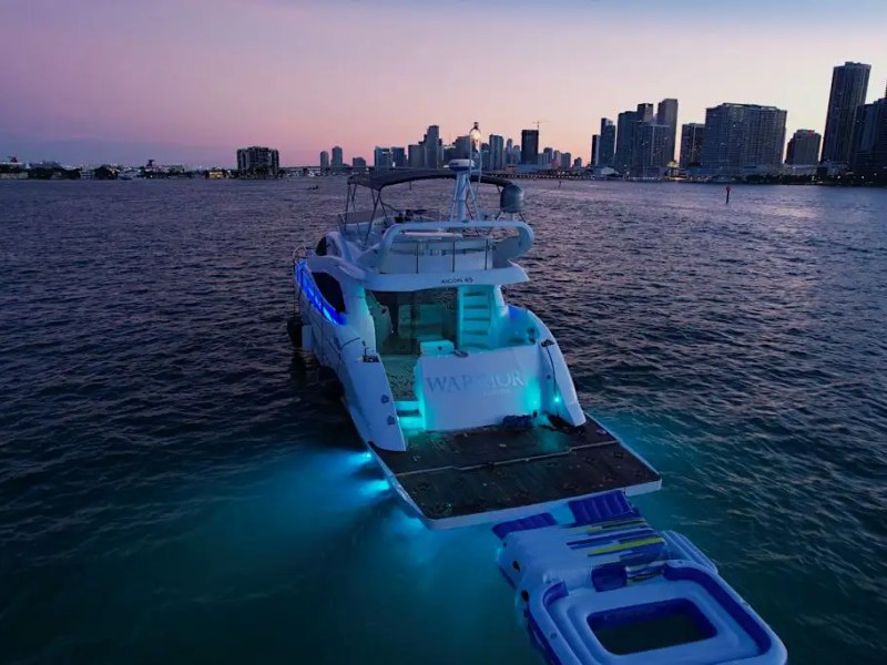 Lit yacht on water at dusk with city skyline in the background.