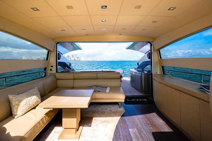 Interior of a yacht with beige seating and a table, ocean view through large windows.