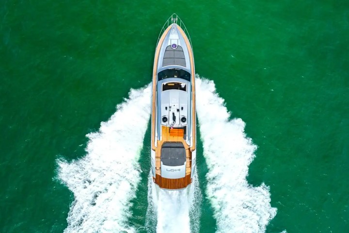 Top view of a yacht moving through green water, leaving a wake behind.