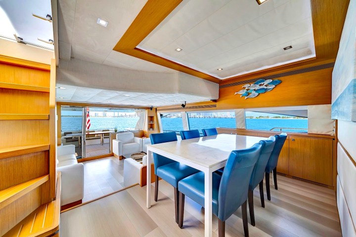 Modern yacht interior with blue chairs, a dining table, and a view of the sea through large windows.