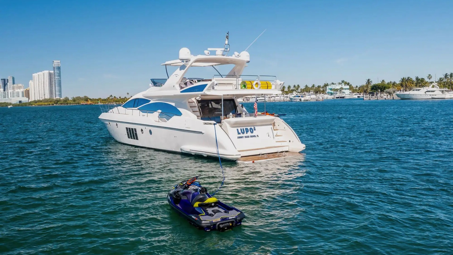 White yacht and a jet ski on blue water with city skyline in the background.