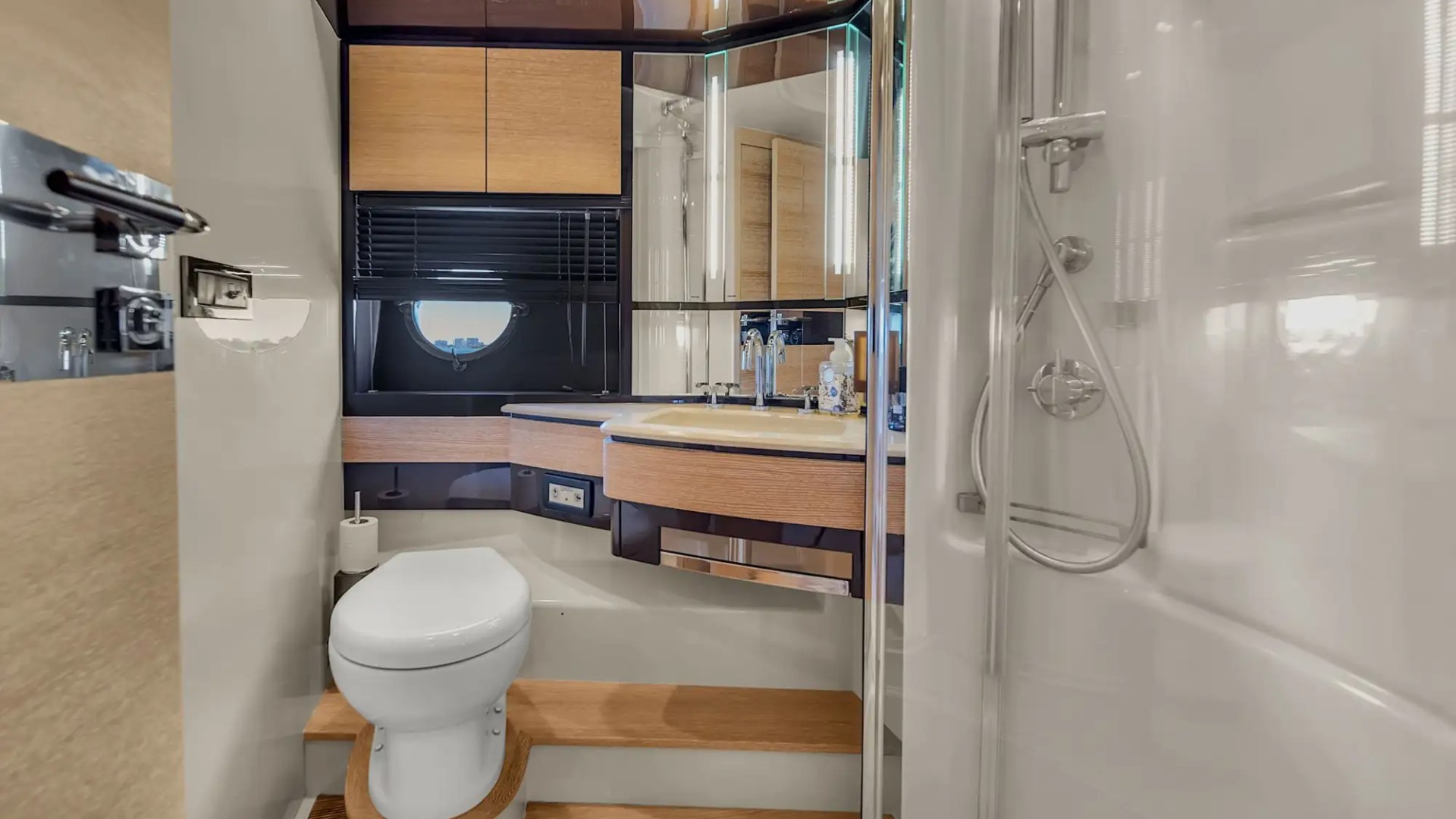 Modern yacht bathroom with toilet, shower, sink, and circular window.