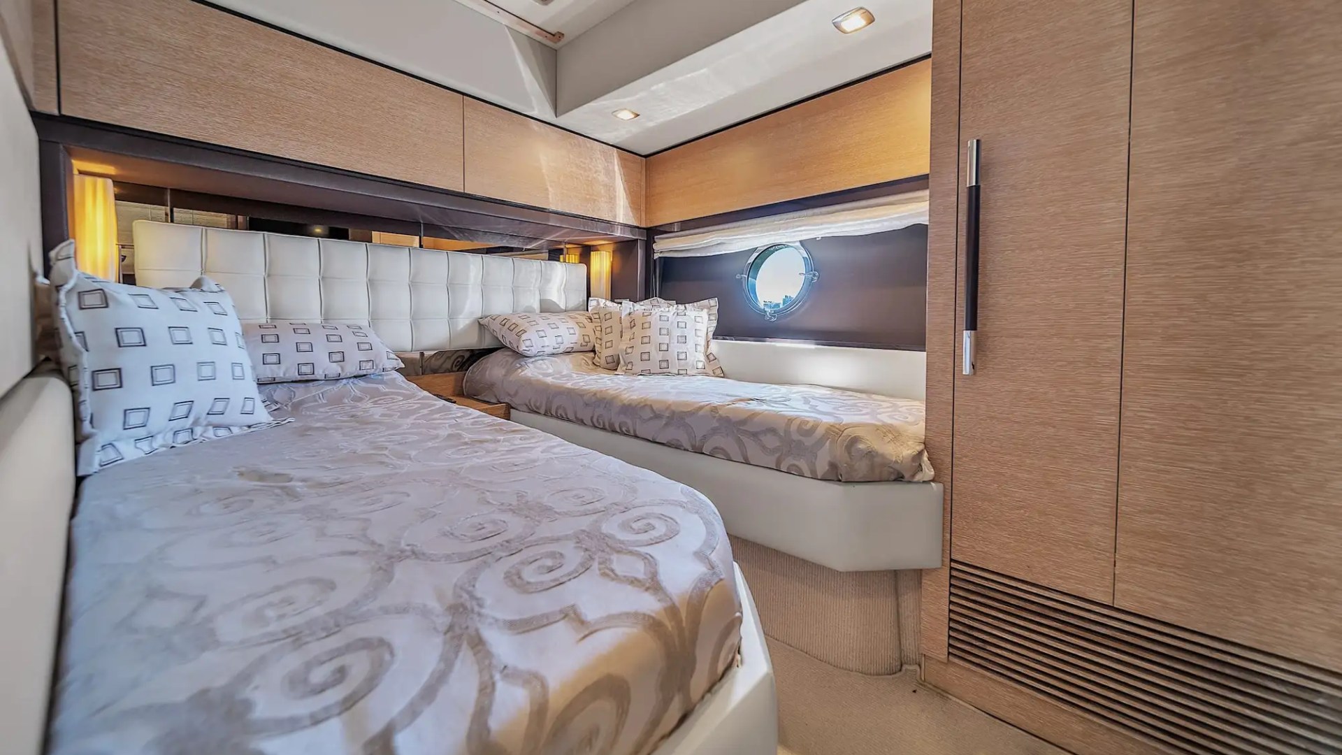 Luxurious cabin with two beds, cushioned headboards, elegant bedding, and a small round window on a yacht.