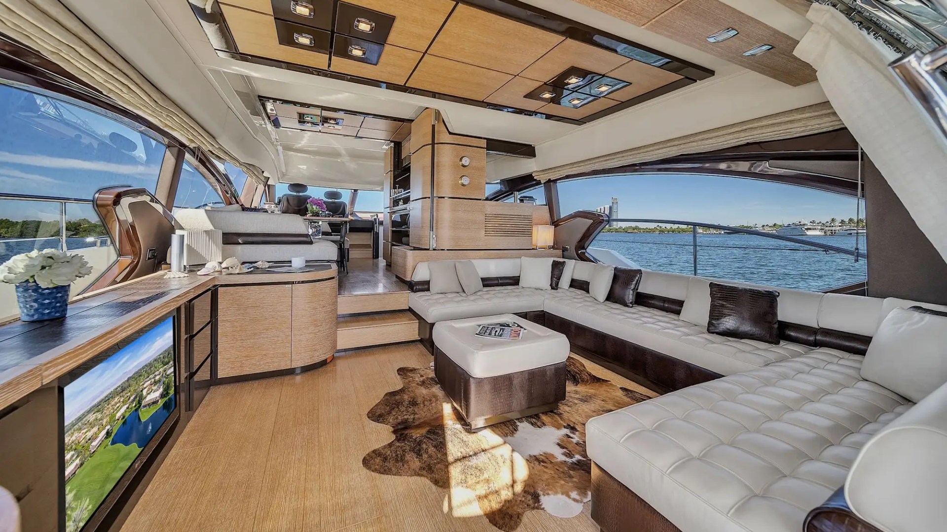 Luxury yacht interior with white leather seating, TV, and ocean view through large windows.