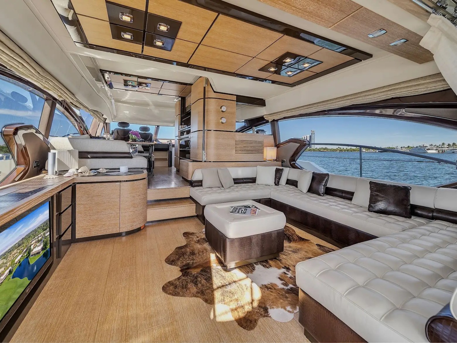 Luxury yacht interior with white leather seating, TV, and ocean view through large windows.