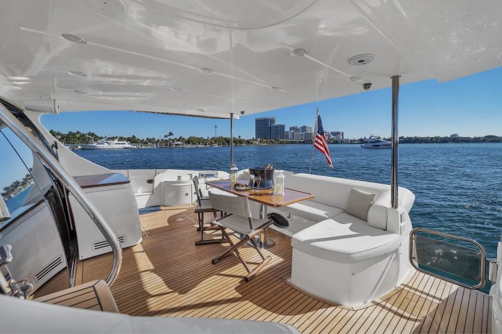 Yacht deck with seating, table, and American flag, overlooking city skyline and water.