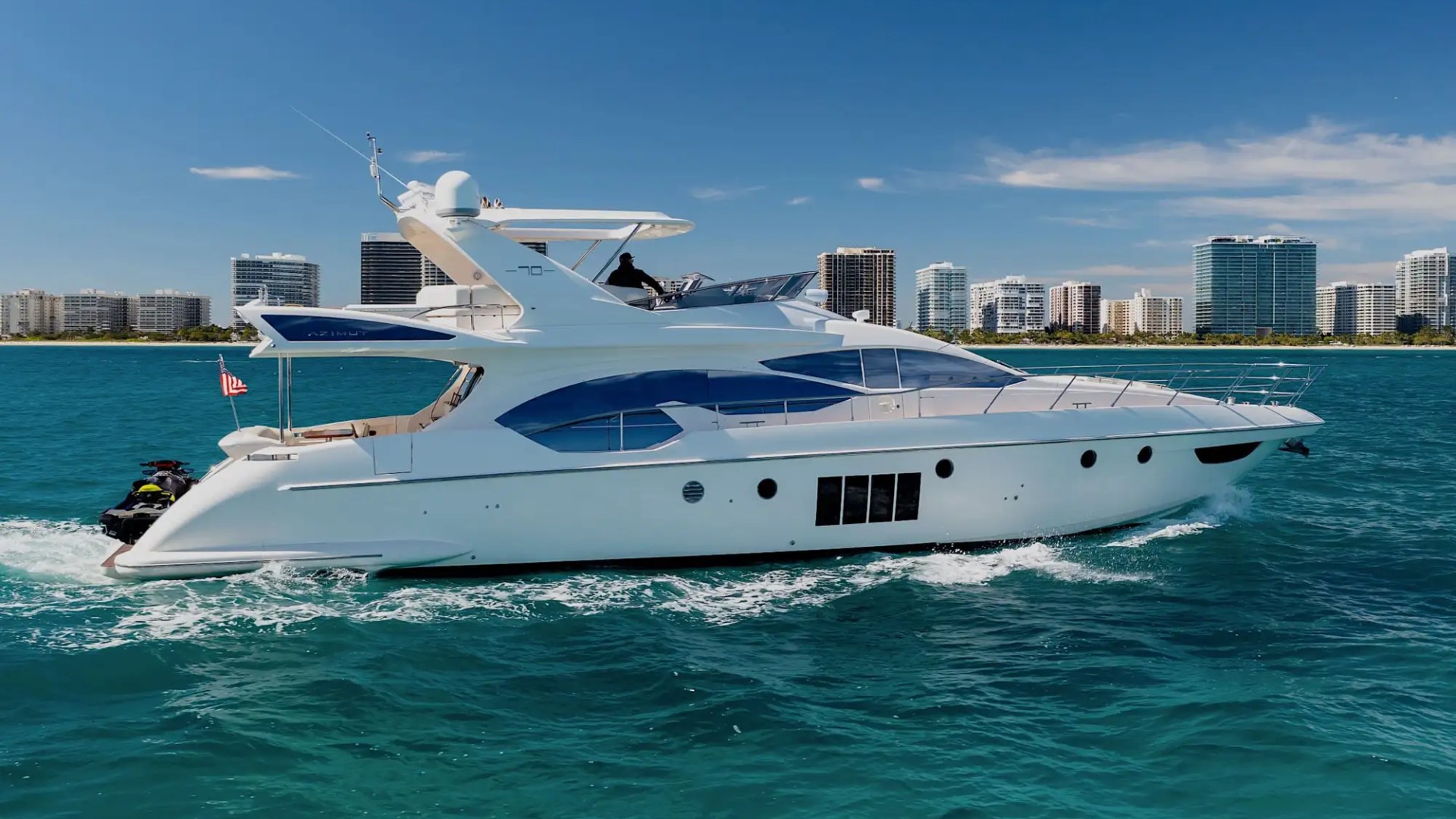 Luxury yacht cruising in blue water with city skyline in the background.