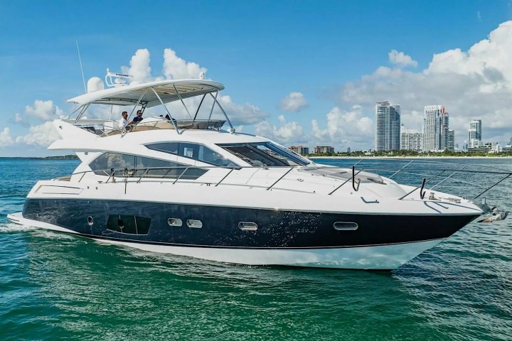 Luxury yacht cruising on clear water with city skyline and blue sky in the background.