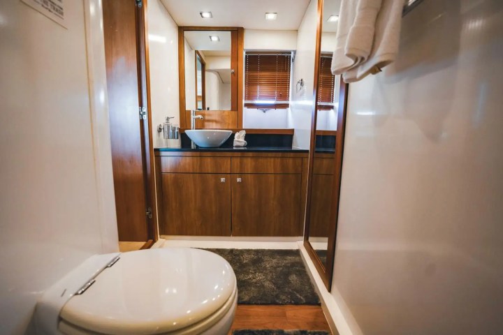 Modern bathroom with wooden cabinets, vessel sink, toilet, and window blinds.