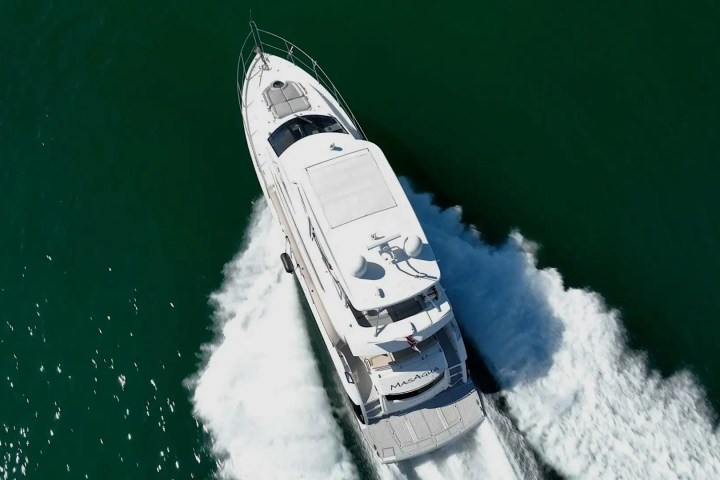Aerial view of a white motor yacht creating a wake on green water.