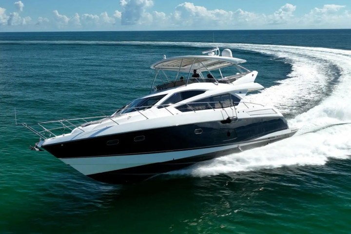 A motor yacht cruising swiftly on clear ocean waters with a clear sky.