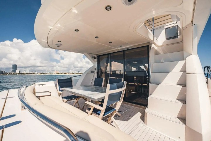 Luxury yacht deck with table, chairs, and cityscape view in the distance.
