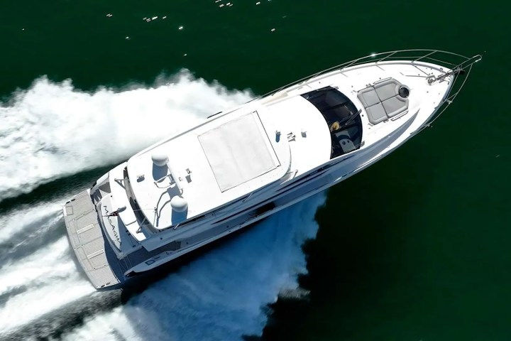 Aerial view of a white motorboat speeding on dark green water, creating a wake behind it.
