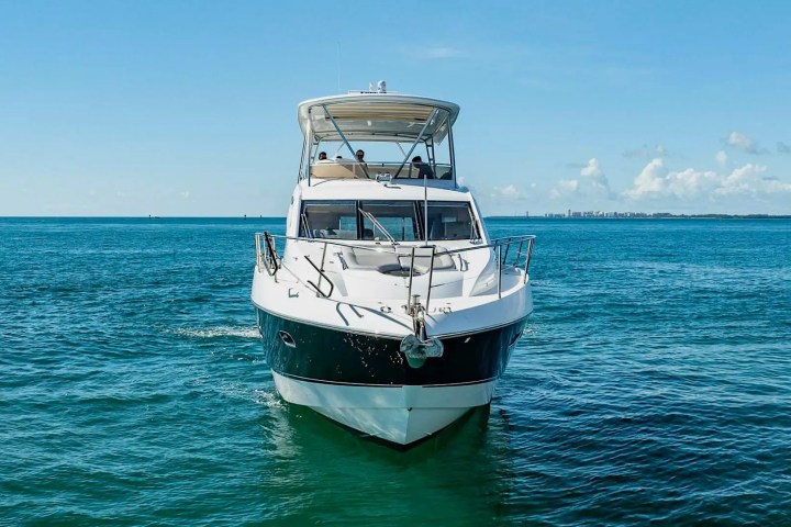 A boat on open ocean with blue sky and distant city skyline.